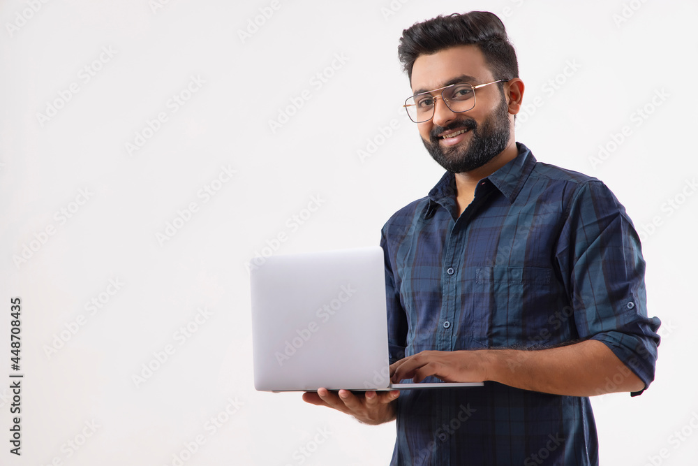 A BEARDED MAN LOOKING AT CAMERA WHILE HOLDING LAPTOP