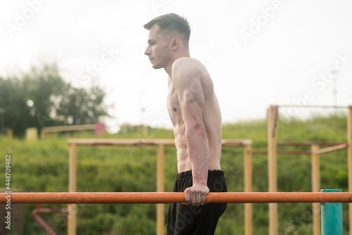Young attractive Caucasian man doing push ups on the bars. Workout concept