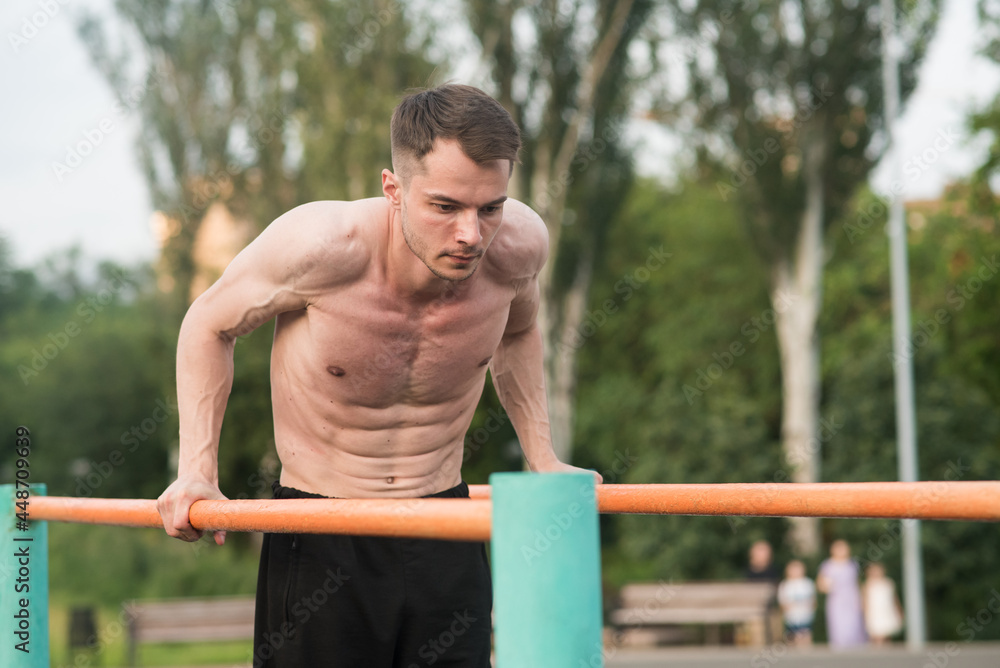 Obraz premium Young attractive Caucasian man doing push ups on the bars. Workout concept