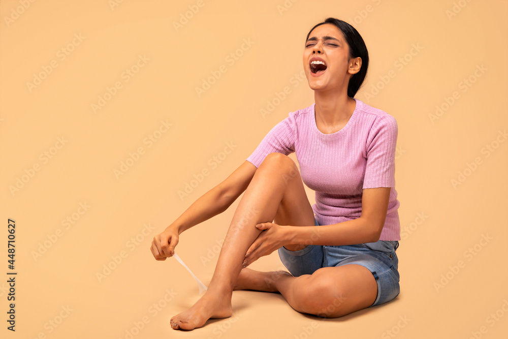Obraz premium A young woman using wax strips on her legs to remove body hair.