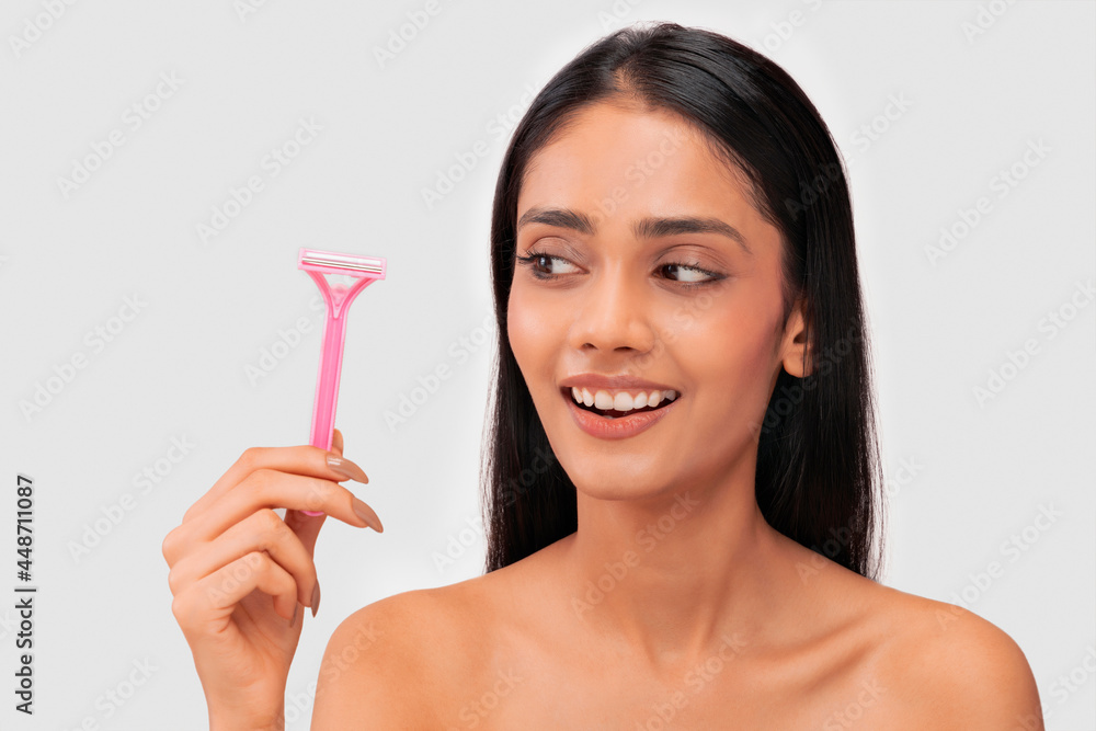 A young woman with clear,spotless skin looking at a hair removal razor. A young woman with clear,spotless skin looking at a hair removal razor.