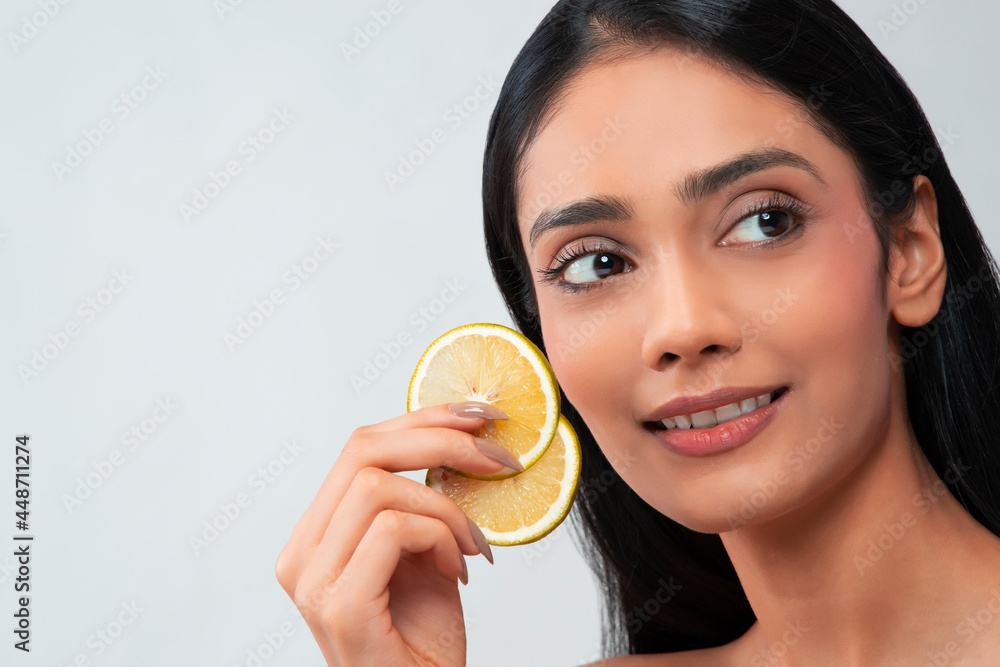 A young woman with clear,spotless skin holding two slices of lemon. A young woman with clear,spotless skin holding two slices of lemon.