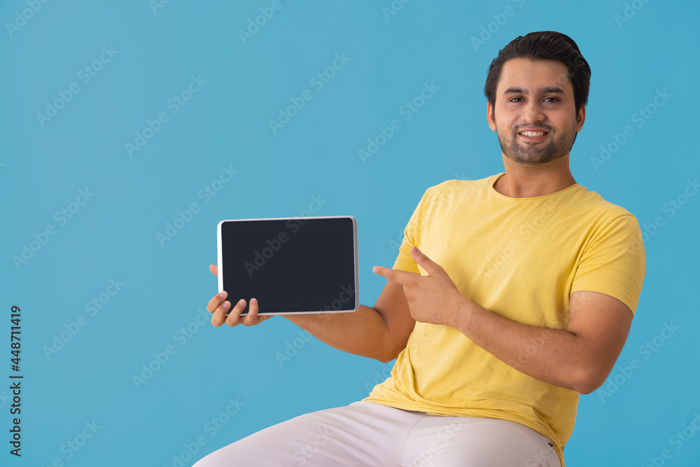 A young man pointing towards a tablet phone in his hands. A young man pointing towards a tablet phone in his hands.