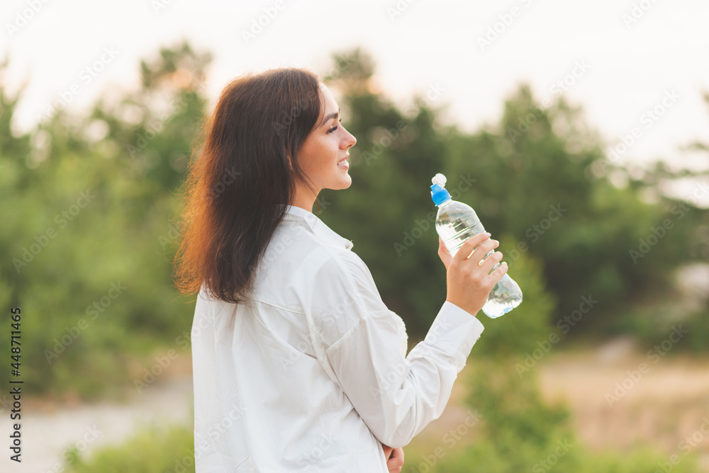 Girl drinks water from a plastic bottle.young caucasian woman in nature forest in woods while holding bottle of water Girl drinks water from a plastic bottle.young caucasian woman in nature forest in woods while holding bottle of water