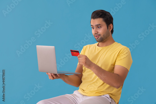 A young man looking at his credit card and latop in a surpised manner. photo