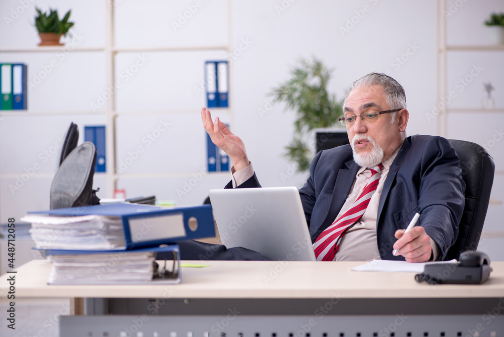Old male employee sitting at workplace Old male employee sitting at workplace