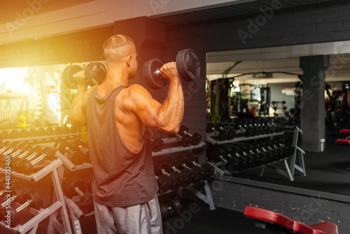 Young fit man in a gym exercising with dumbbells.healthy man working out with dumbbells.Copy space.