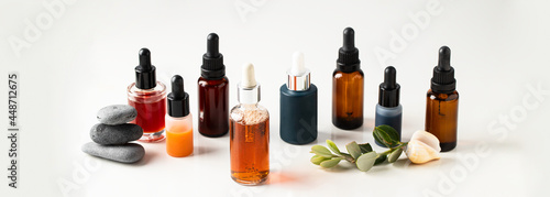 Different crystal bottles with bio serum, natural oil and cream on white background with plabt and stown, Large image for banner.