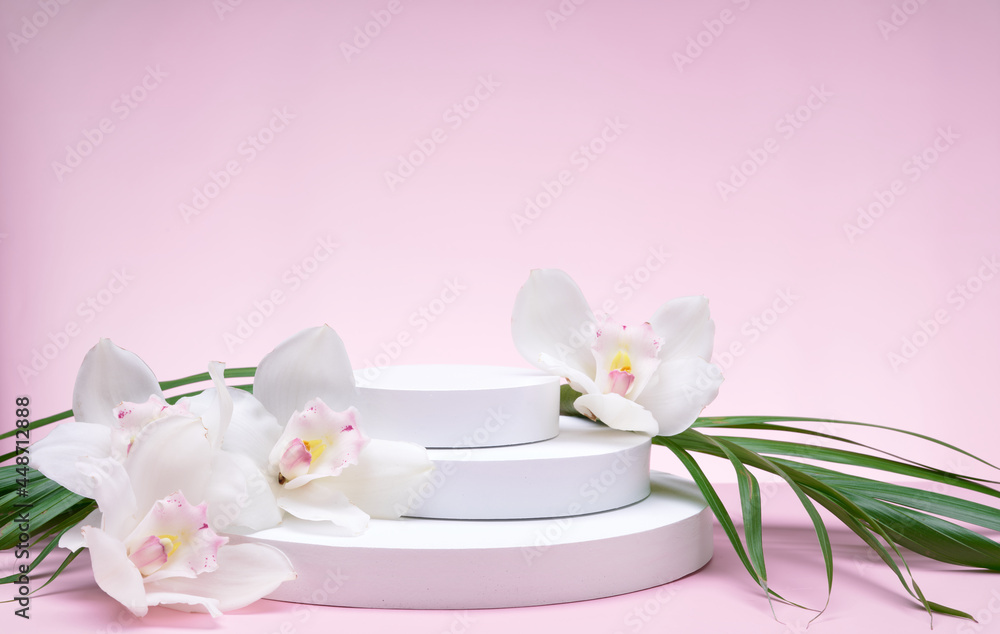 White geometric shapes podium for product display on pink background with orchid flowers and palm leaves. Monochrome stage, stand for product promotion in minimal style.