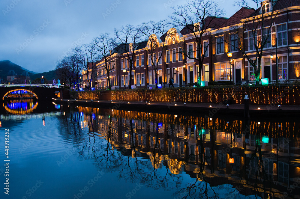 Fototapeta premium ライトアップされた長崎ハウステンボスの奥に橋が見える川と町並みの夕暮れ