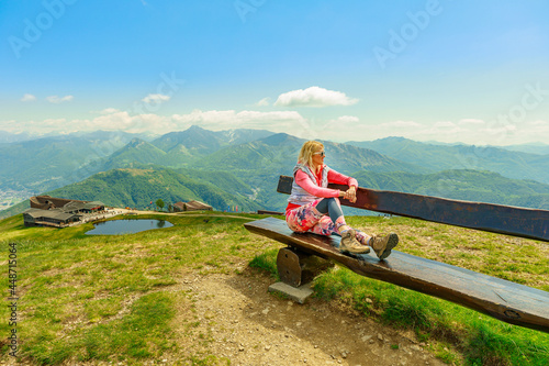 Backpacker woman in a trekking dress enjoying Tamaro mount in Switzerland. Swiss bench by the pond in Foppa alp in Ticino canton. Top of Rivera station of cable car. photo