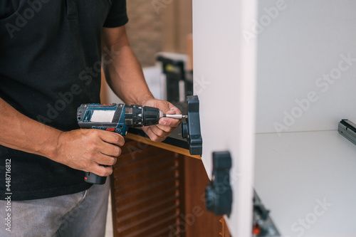 Man attaching a piece in a furniture using a drill in a workshop