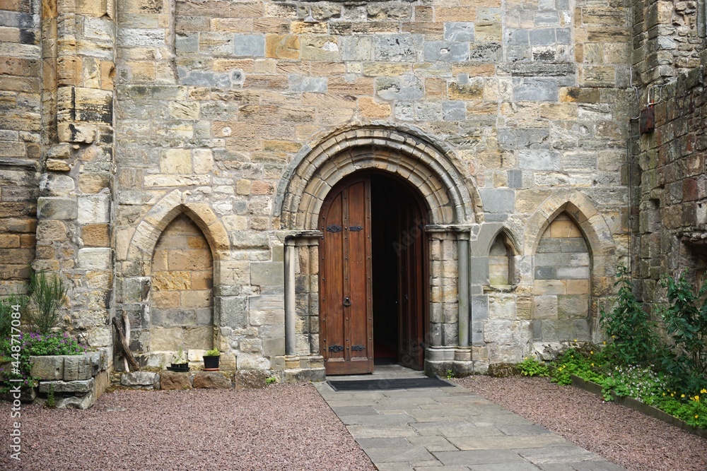 Arched doorway with half open door in ancient medieval European stone wall