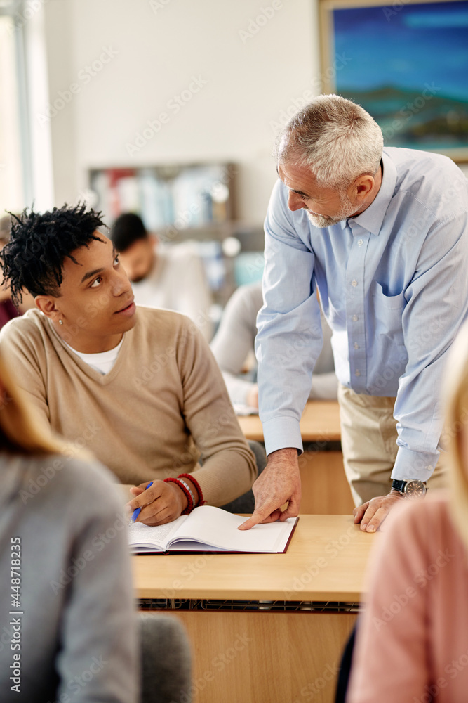 Young black student talking to his professor who is assisting him with lecture in classroom. Young black student talking to his professor who is assisting him with lecture in classroom.