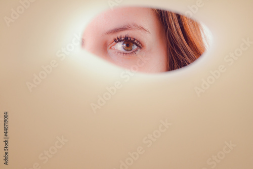 An eye of the lady who is peeping through a hole of paper with space for advertising