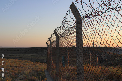 Barbed wire on sunset. Spiky wire fence. Prison barbed fence. Airport security fence after sunset. National border. Barbed Wire Fence in a military base. Area with barbed wire. Dangerous area.