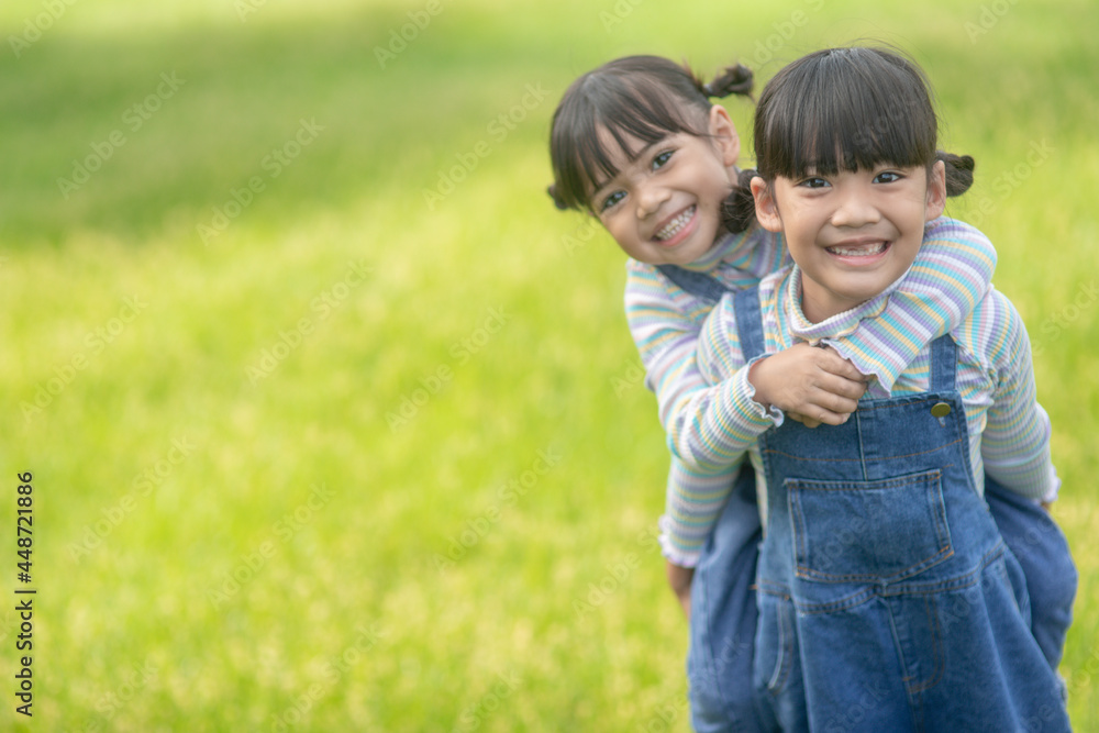 Fototapeta premium Asian Little girl with elder sister at a park riding on her back