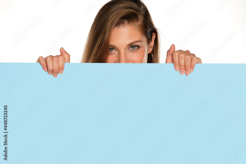a young advertizing smiling woman peeks behind a empty board a young advertizing smiling woman peeks behind a empty board