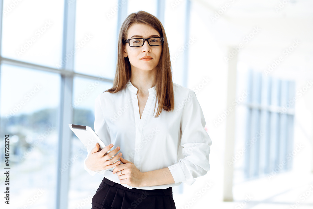 Beautiful female specialist with dark hair standing in modern office and smiling charmingly. Working on design, data analysis, plan strategy. Business people concept Beautiful female specialist with dark hair standing in modern office and smiling charmingly. Working on design, data analysis, plan strategy. Business people concept