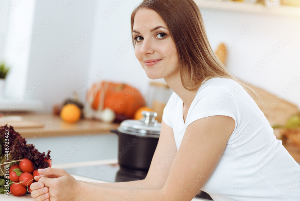 An attractive young woman ready to cook a new recipe for a delicious salad mix while sitting at the table in sunny kitchen