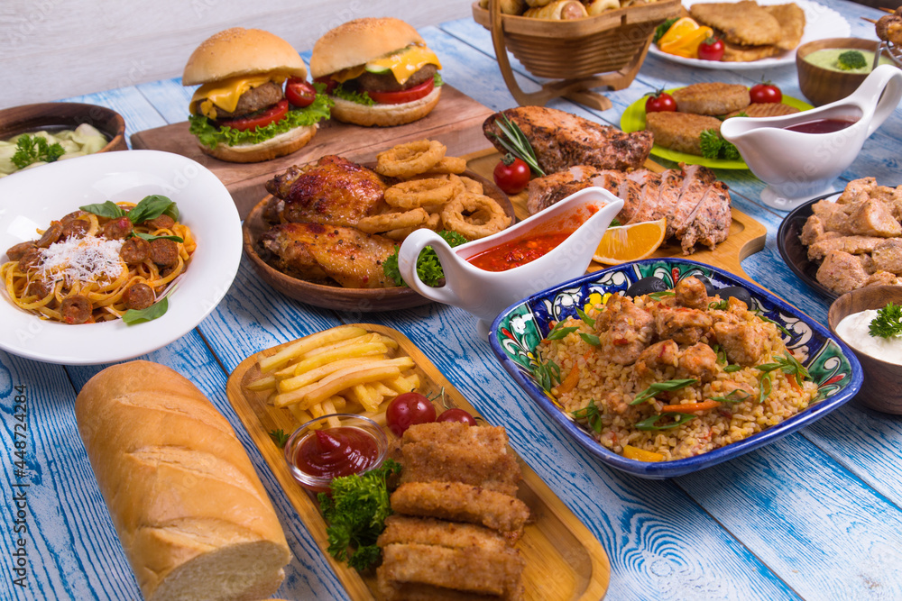 Wooden table full of delicious grilled bbq and fried food. Meat and vegetables. Summer picnic background. Delicious dinner. Wooden table full of delicious grilled bbq and fried food. Meat and vegetables. Summer picnic background. Delicious dinner.