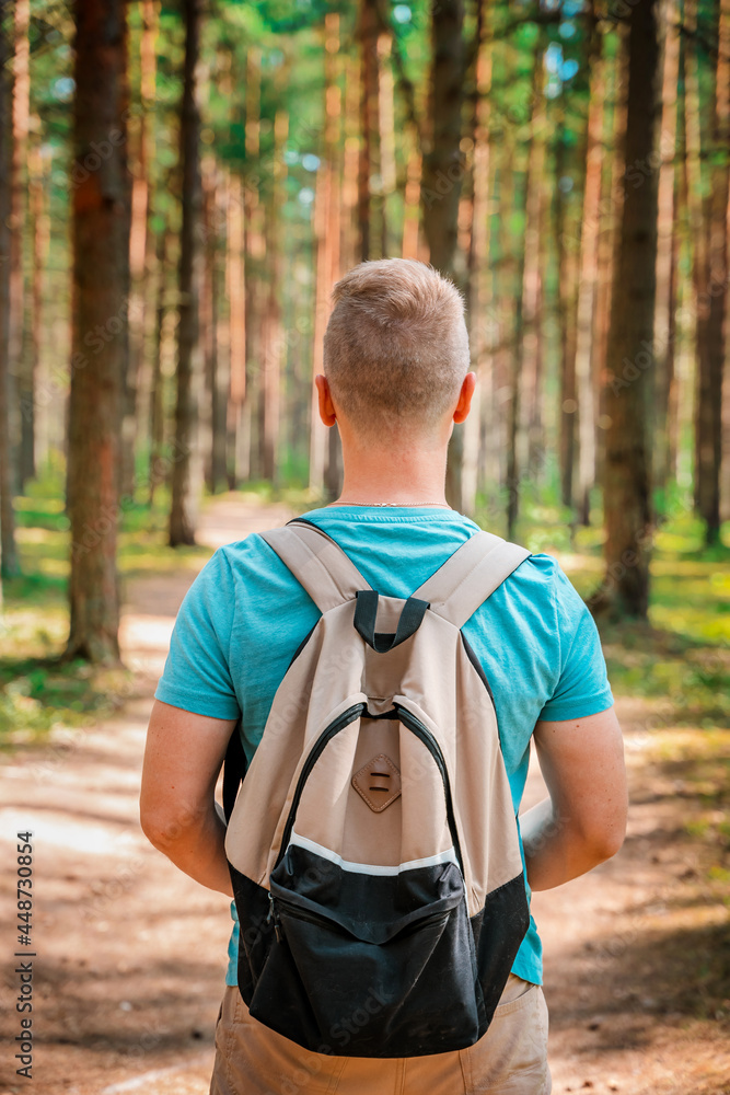 A young man with a backpack walks through a pine summer forest A young man with a backpack walks through a pine summer forest