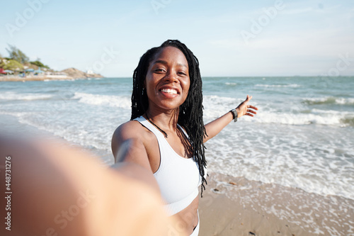 Canvastavla Pretty young woman with dreadlocks smiling and taking selfie on beach