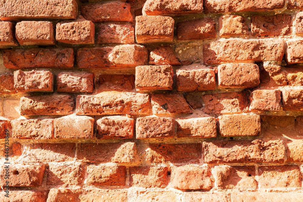 Obraz premium Fragment of a brick ruin wall. The red brick has partially collapsed over time and under the influence of weather. The surface has numerous depressions. Background. Texture.