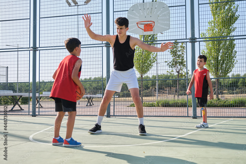 Three brothers playing basketball, one of them has a leg prosthesis.