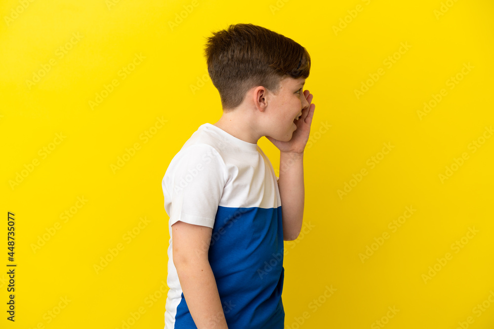 Little redhead boy isolated on yellow background shouting with mouth wide open to the side Little redhead boy isolated on yellow background shouting with mouth wide open to the side