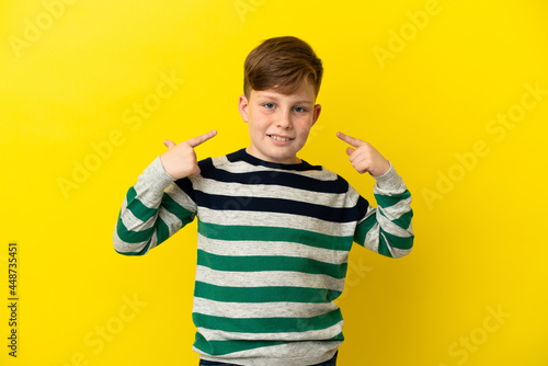 Little redhead boy isolated on yellow background giving a thumbs up gesture