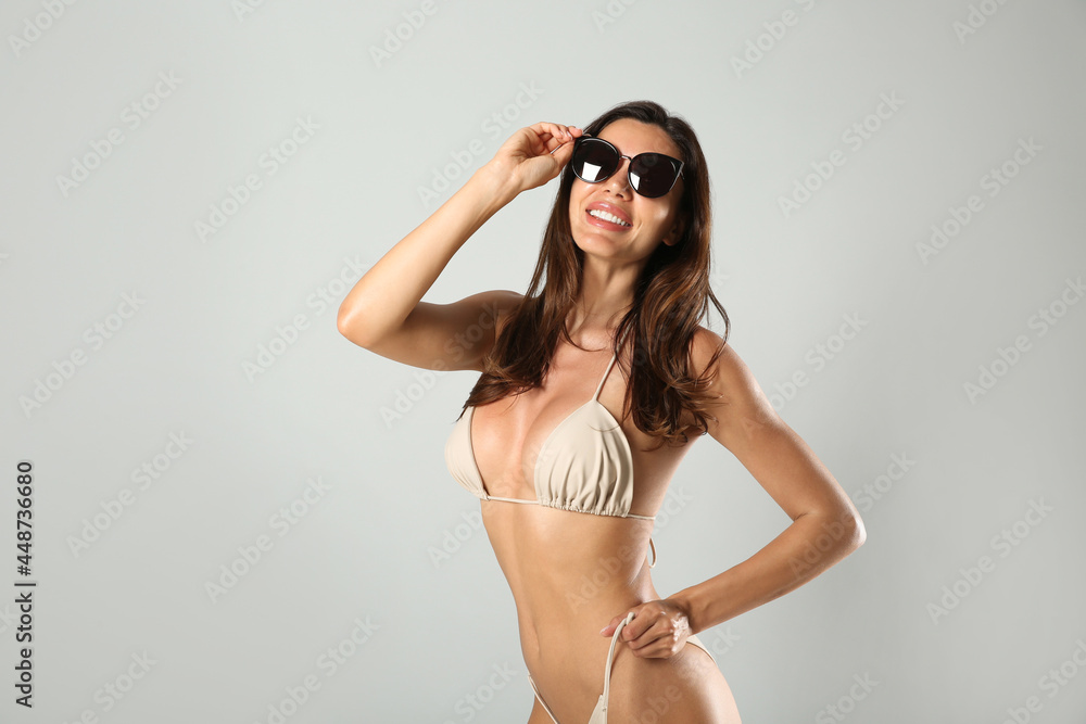 Beautiful woman in stylish bikini and sunglasses on light grey background. Space for text Beautiful woman in stylish bikini and sunglasses on light grey background. Space for text