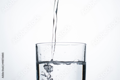Jet of water or alcohol is pouring into a glass with splashes and bubbles, copy space
