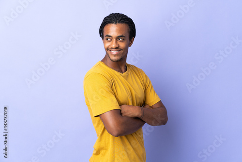 Young African American man with braids man isolated on purple background looking to the side and smiling