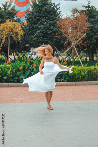 A blonde girl in a white dress and ballerinas gracefully whirls in a chinese park © Irina Flamingo