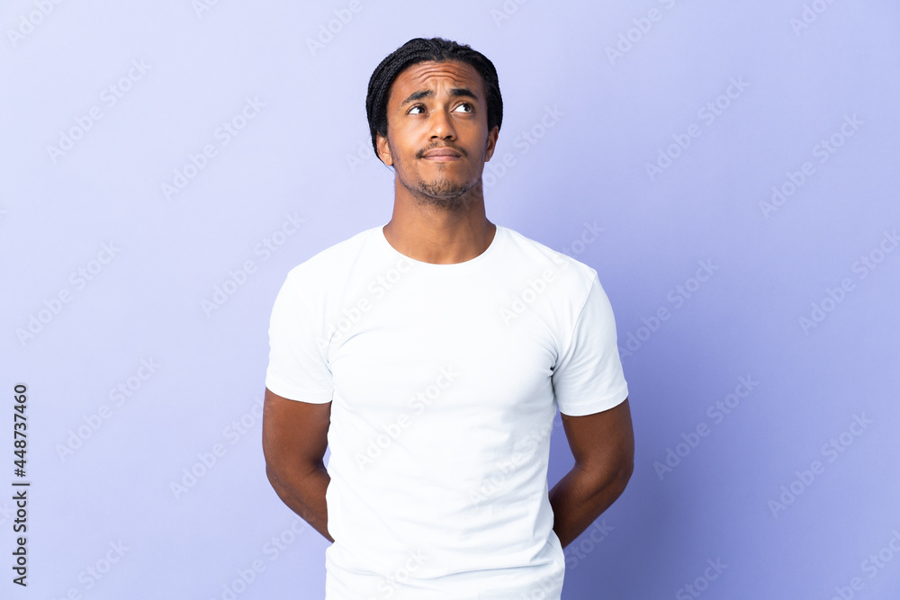 Young African American man with braids man isolated on purple background and looking up Young African American man with braids man isolated on purple background and looking up