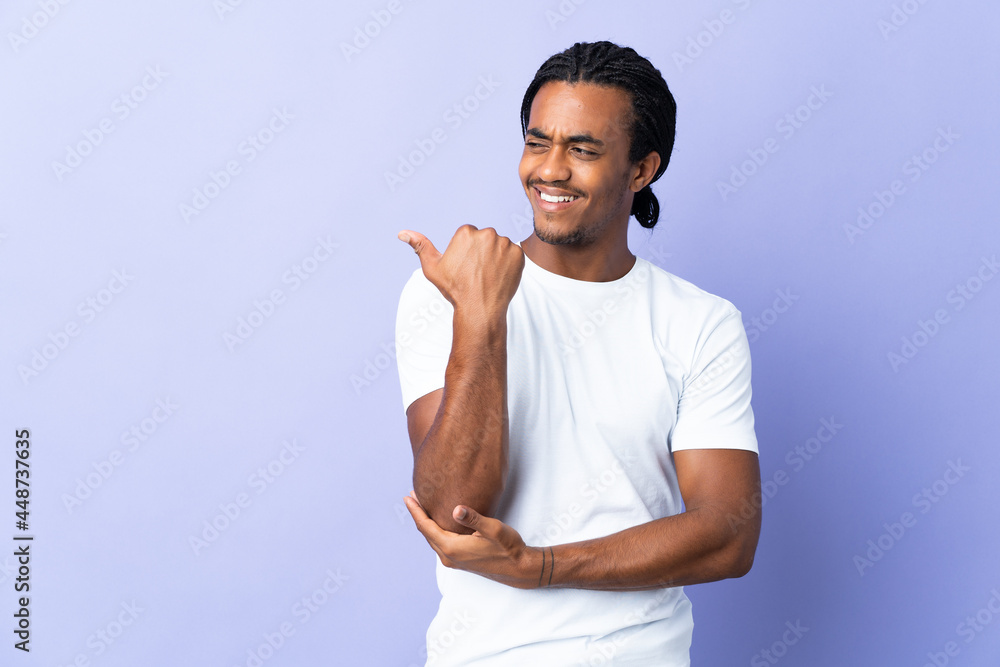 Young African American man with braids man isolated on purple background pointing to the side to present a product Young African American man with braids man isolated on purple background pointing to the side to present a product