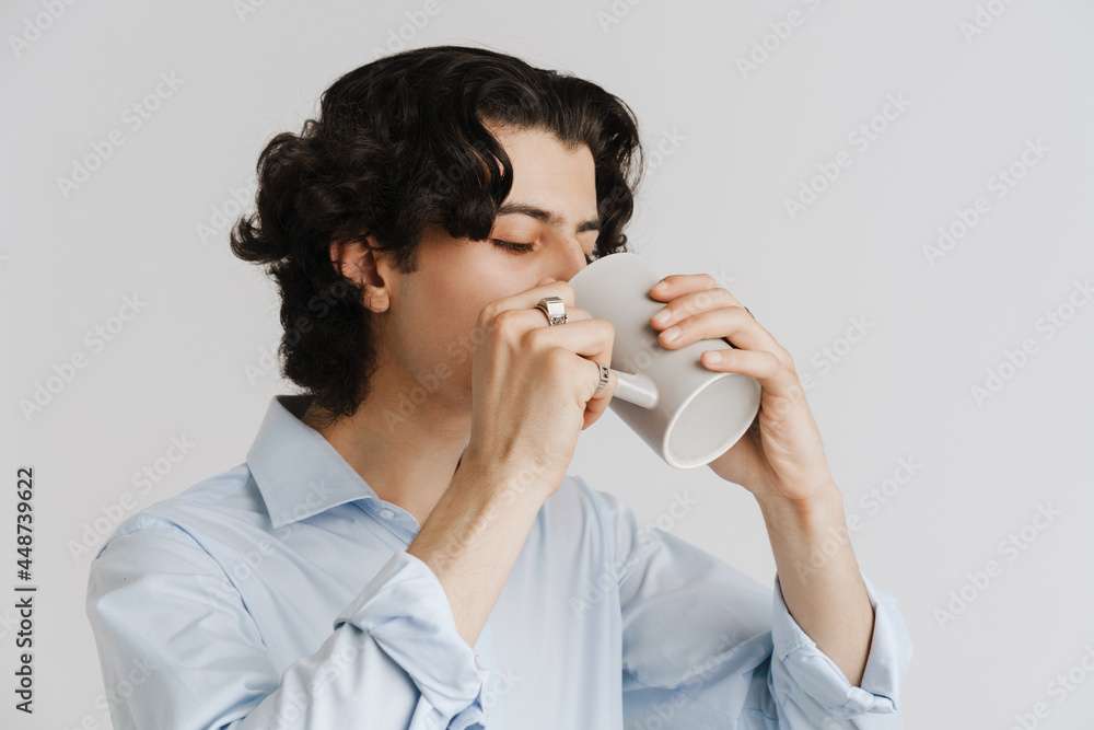 Young brunette man wearing shirt drinking coffee while posing at camera Young brunette man wearing shirt drinking coffee while posing at camera
