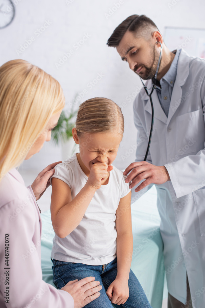 Fototapeta premium Kid sneezing near mother and doctor with stethoscope