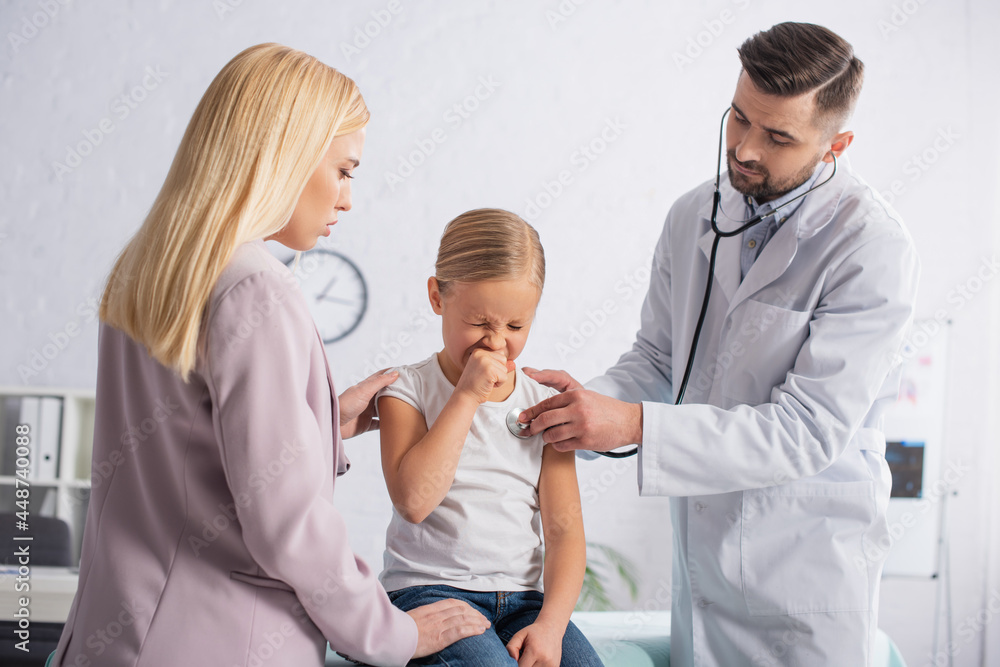 Sick kid sneezing near parent and pediatrician with stethoscope Sick kid sneezing near parent and pediatrician with stethoscope