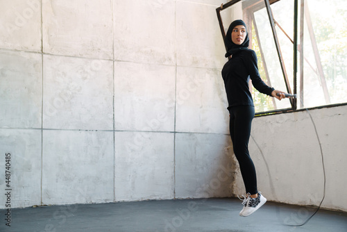 Young muslim sportswoman in hijab working out with jumping rope