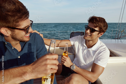 Foto Young male friends drinking beer on yacht in sea