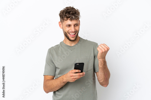 Young caucasian handsome man isolated on white background with phone in victory position