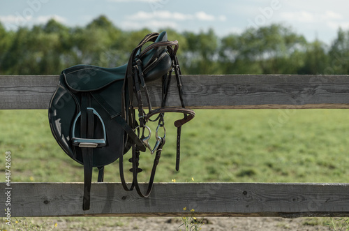 Saddle and bridle are on a wooden fence in outdoors. photo