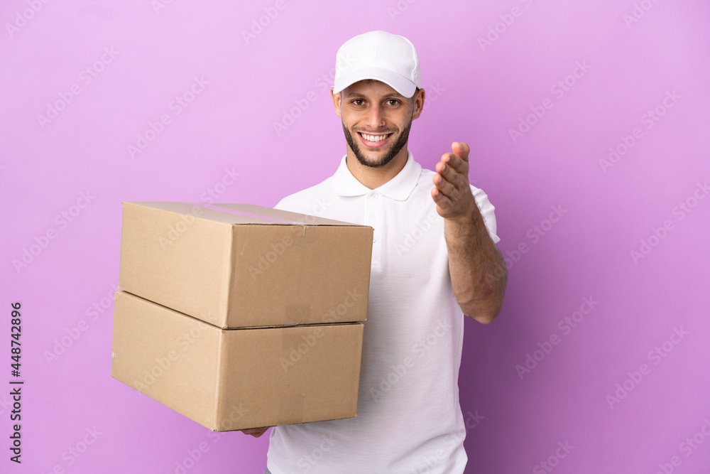 Delivery caucasian man isolated on purple background shaking hands for closing a good deal Delivery caucasian man isolated on purple background shaking hands for closing a good deal