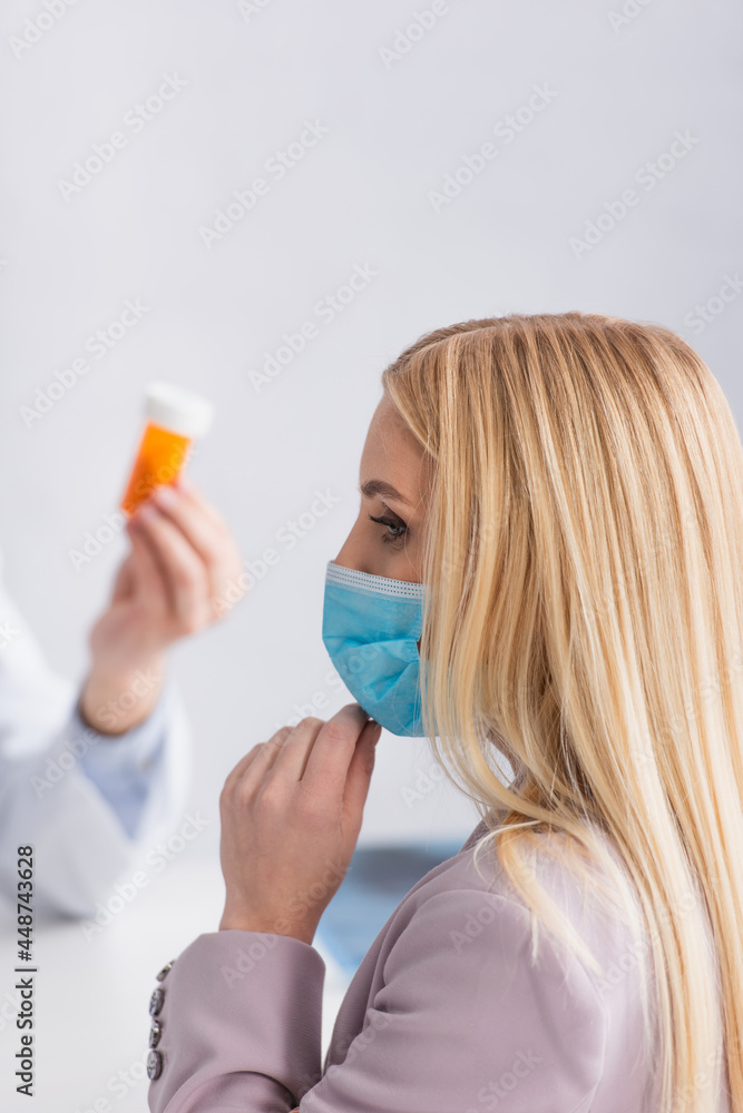 blonde woman in medical mask near doctor with pills container blonde woman in medical mask near doctor with pills container