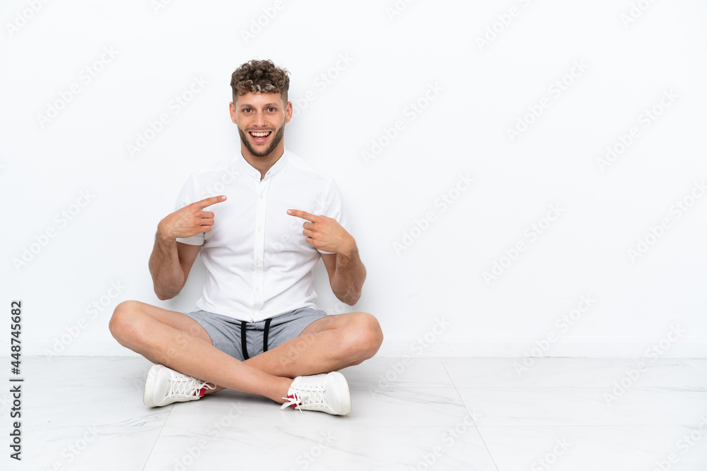 Fototapeta premium Young blonde man sitting on the floor isolated on white background with surprise facial expression