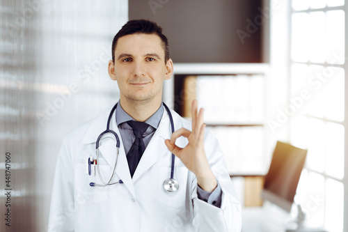 Male doctor standing with thumbs up sign in sunny clinic. Perfect medical service in hospital