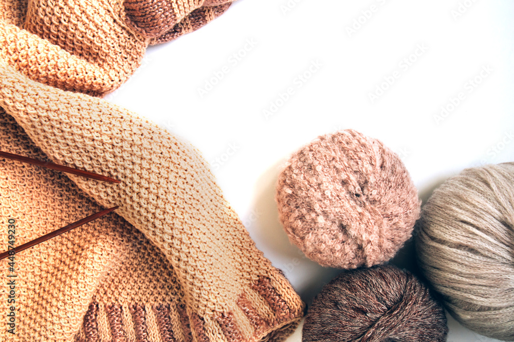 Balls of woolen yarn and a knitted beige sweater, knitting needles on a white background Balls of woolen yarn and a knitted beige sweater, knitting needles on a white background