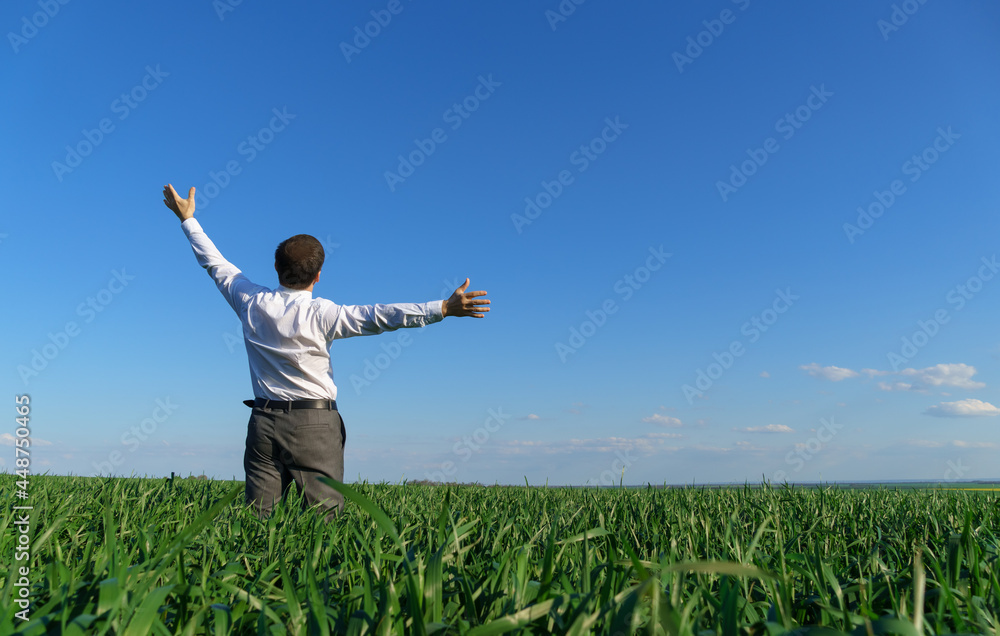businessman poses in a field, he looks into the distance and rests, green grass and blue sky as background businessman poses in a field, he looks into the distance and rests, green grass and blue sky as background